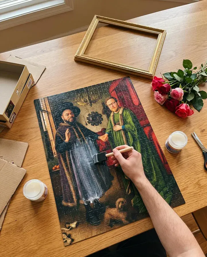 Glue being brushed onto a finished puzzle of a couple painted as The Arnolfini Portrait, beside a gold frame and roses